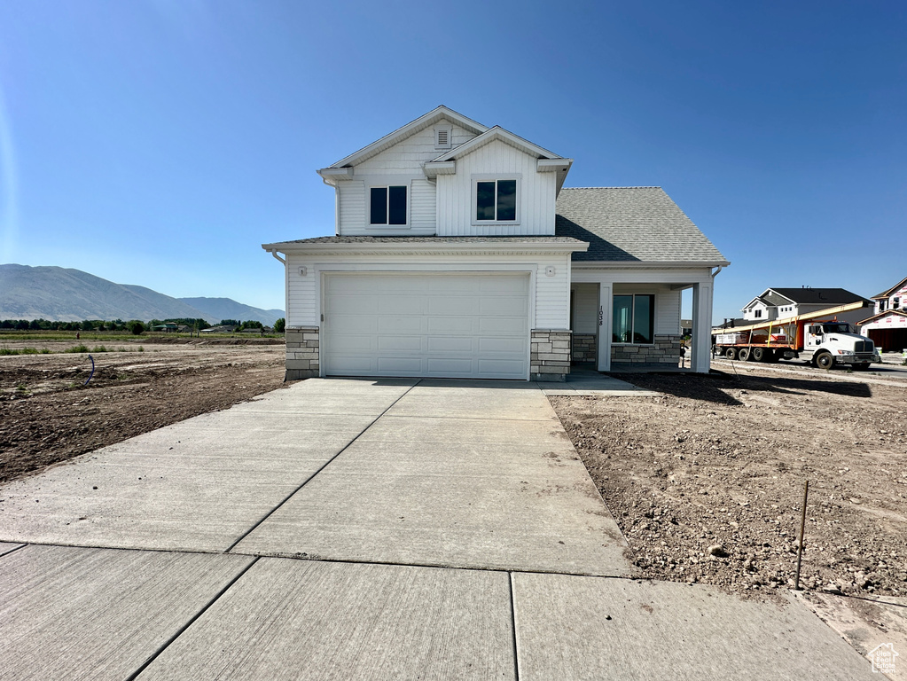 View of front of home featuring driveway, a mountain view, an attached garage, stone siding, and a porch