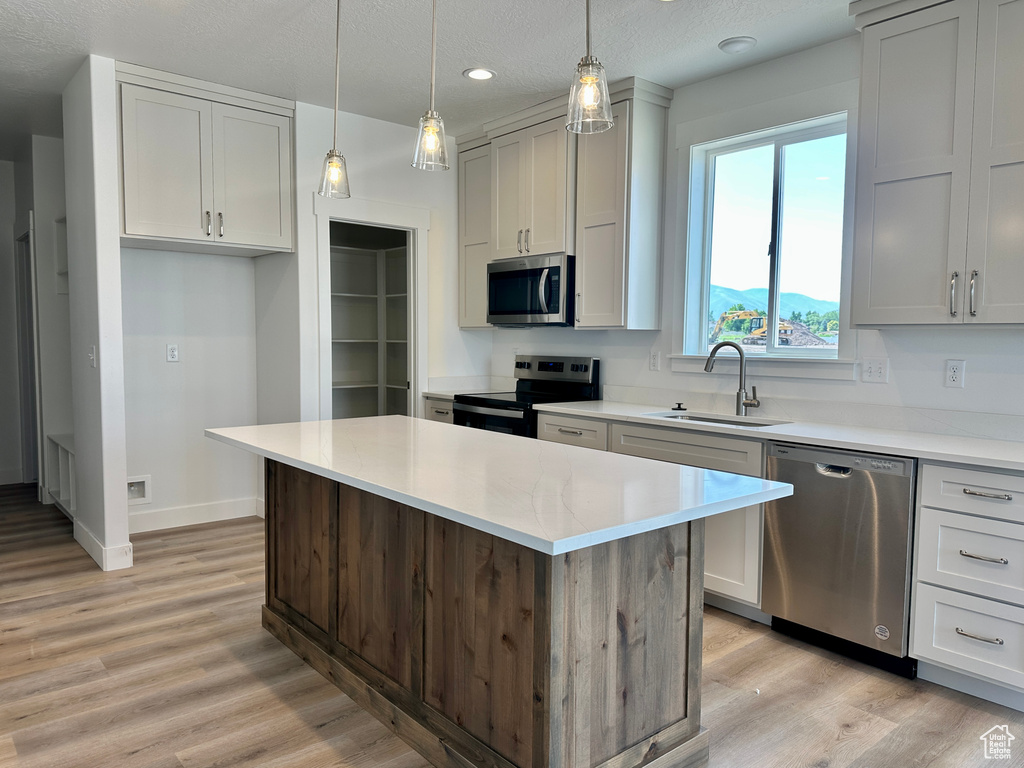 Kitchen with appliances with stainless steel finishes, light wood-style flooring, a kitchen island, recessed lighting, and a textured ceiling