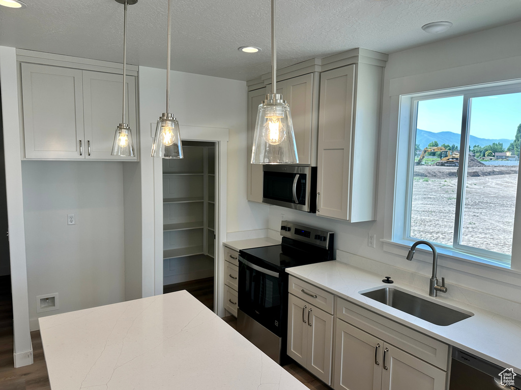 Kitchen featuring stainless steel appliances, light countertops, a textured ceiling, hanging light fixtures, and recessed lighting