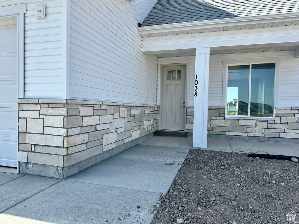 Property entrance with stone siding, roof with shingles, and a porch