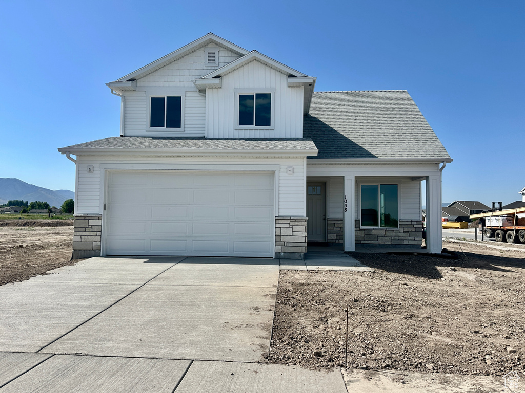 View of front of home with concrete driveway, a garage, stone siding, and a porch