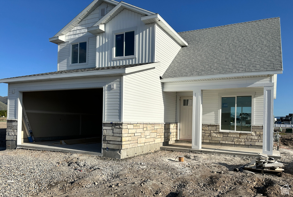 View of front of property featuring a porch, stone siding, roof with shingles, and a garage