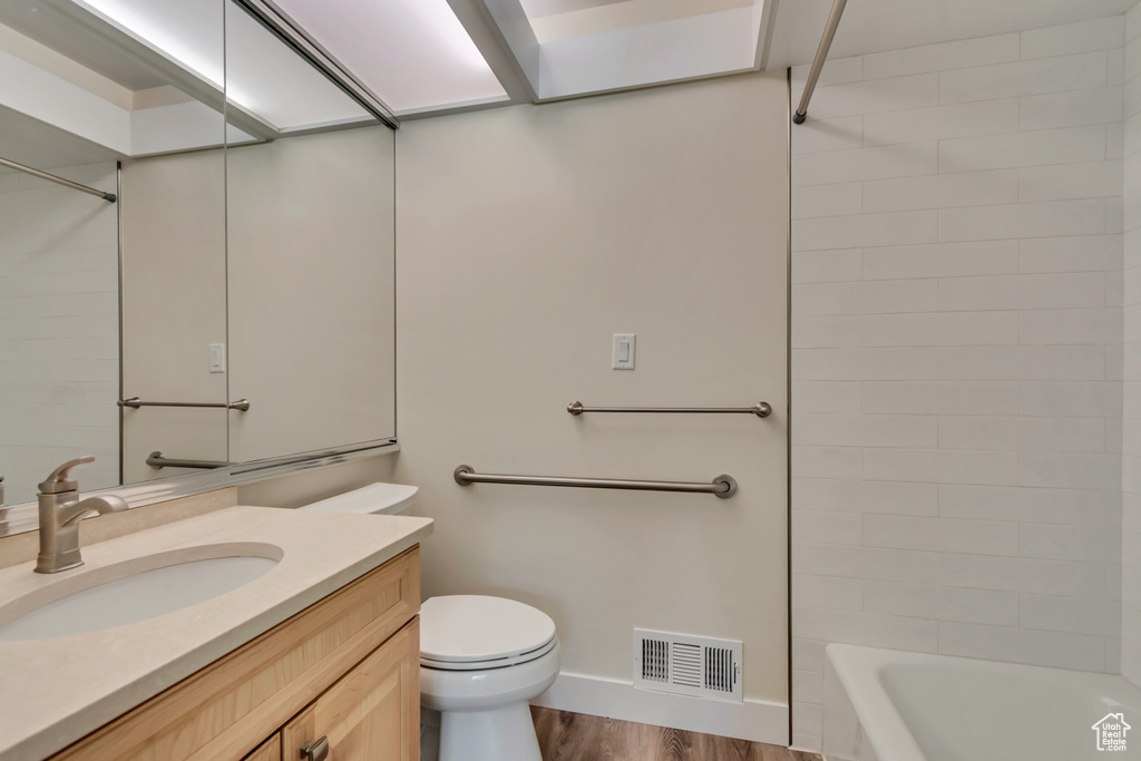 Full bath with toilet, vanity, wood finished floors, baseboards, and tub / shower combination