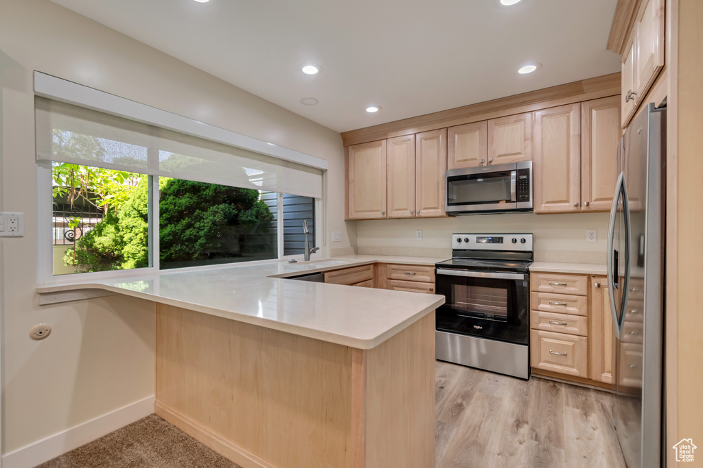 Kitchen featuring appliances with stainless steel finishes, light brown cabinets, a peninsula, light countertops, and recessed lighting