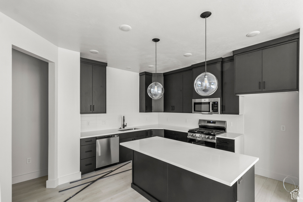 Kitchen featuring dark cabinets, stainless steel appliances, light countertops, a sink, and pendant lighting