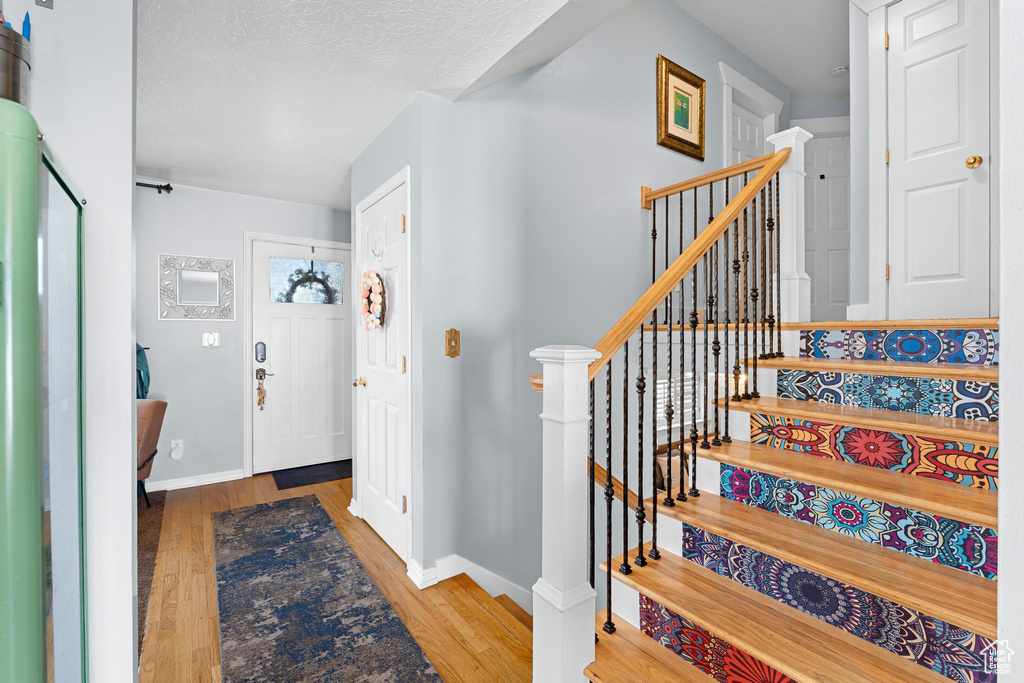 Entryway with stairway, baseboards, a textured ceiling, and wood finished floors