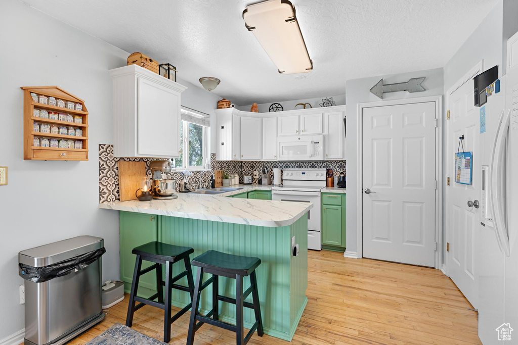 Kitchen with white cabinets, white appliances, light wood-type flooring, and a peninsula