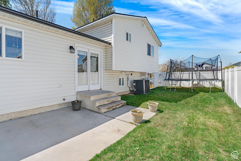 Back of house with cooling unit, a yard, a patio area, fence, and a trampoline