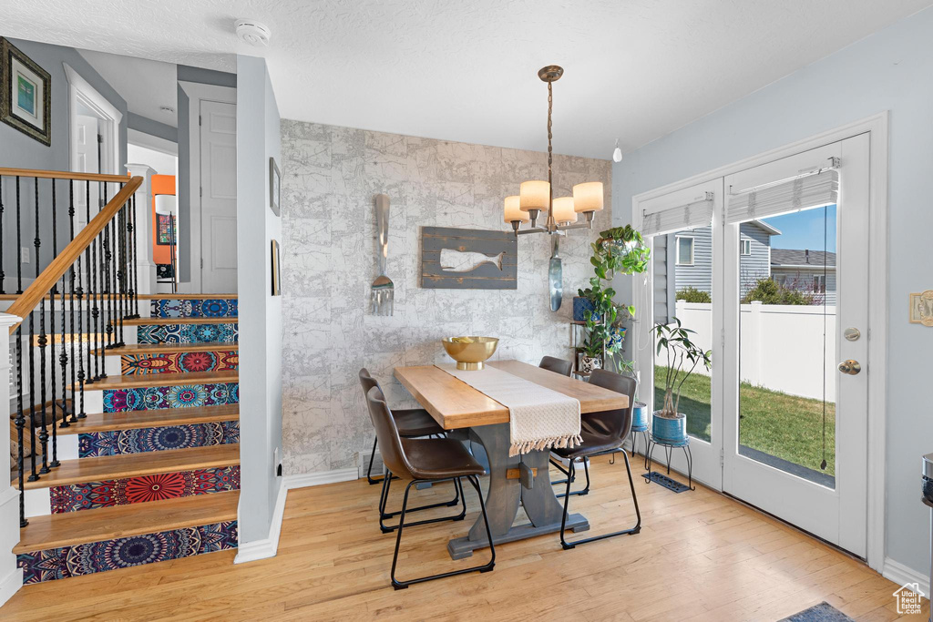 Dining room with wood finished floors, an inviting chandelier, an accent wall, and stairway
