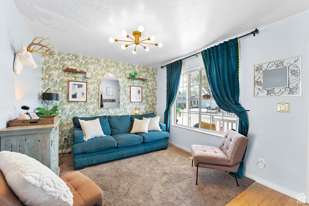 Living area featuring baseboards, wallpapered walls, a chandelier, a textured ceiling, and an accent wall