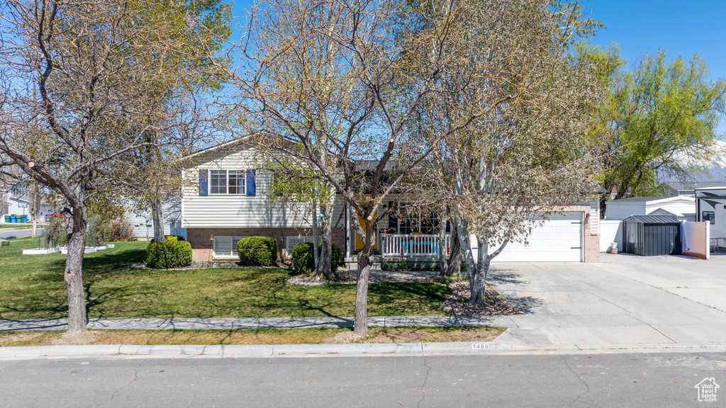 Tri-level home featuring a garage, a porch, a front lawn, brick siding, and driveway