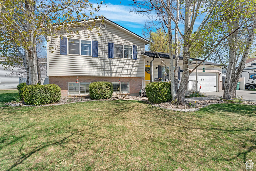 Split level home with a front yard, an attached garage, brick siding, and driveway