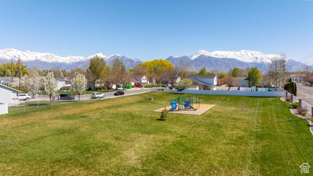 Exterior space with a mountain view, fence, a playground, and a lawn