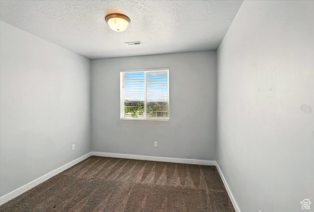 Unfurnished room with dark carpet, baseboards, and a textured ceiling