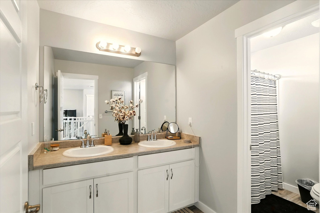 Bathroom with double vanity, baseboards, curtained shower, and toilet