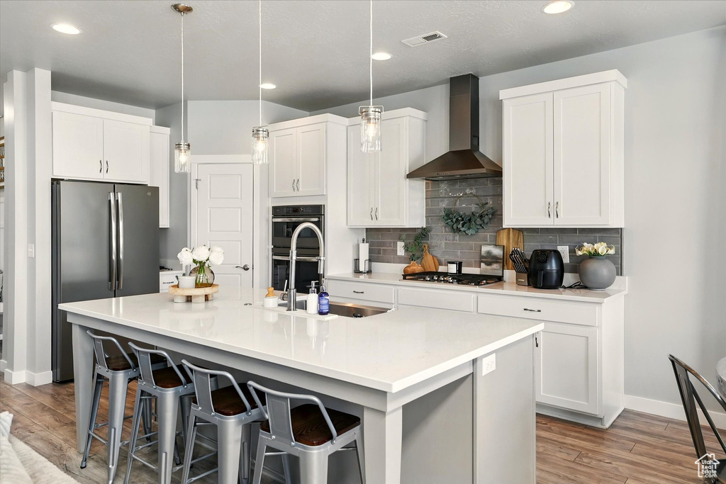 Kitchen featuring wall chimney exhaust hood, stainless steel appliances, decorative backsplash, light wood-style flooring, and recessed lighting