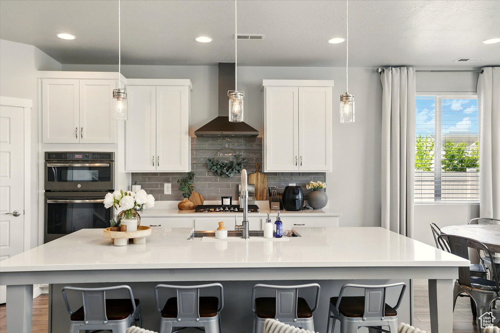 Kitchen with wall chimney range hood, backsplash, a kitchen bar, white cabinetry, and recessed lighting