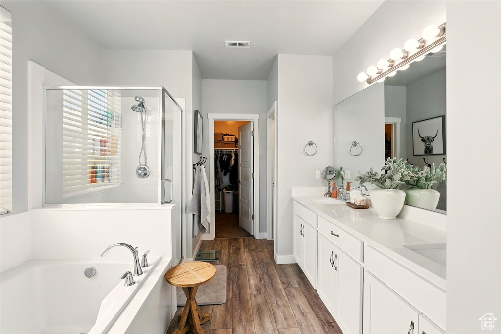 Bathroom with a shower stall, a bath, wood finished floors, a walk in closet, and double vanity