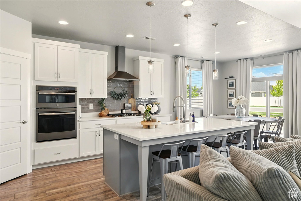 Kitchen featuring a sink, wall chimney exhaust hood, stainless steel double oven, a kitchen breakfast bar, and gas cooktop