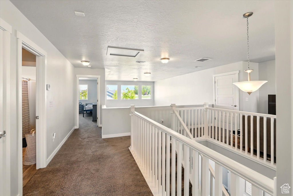 Hall with baseboards, dark carpet, an upstairs landing, and a textured ceiling