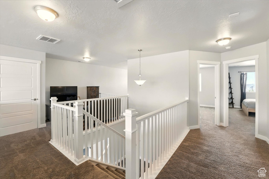 Hallway featuring an upstairs landing, carpet, baseboards, and a textured ceiling