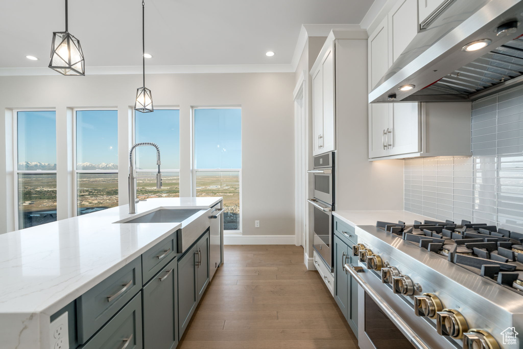 Kitchen featuring stainless steel appliances, a sink, under cabinet range hood, white cabinetry, and ornamental molding