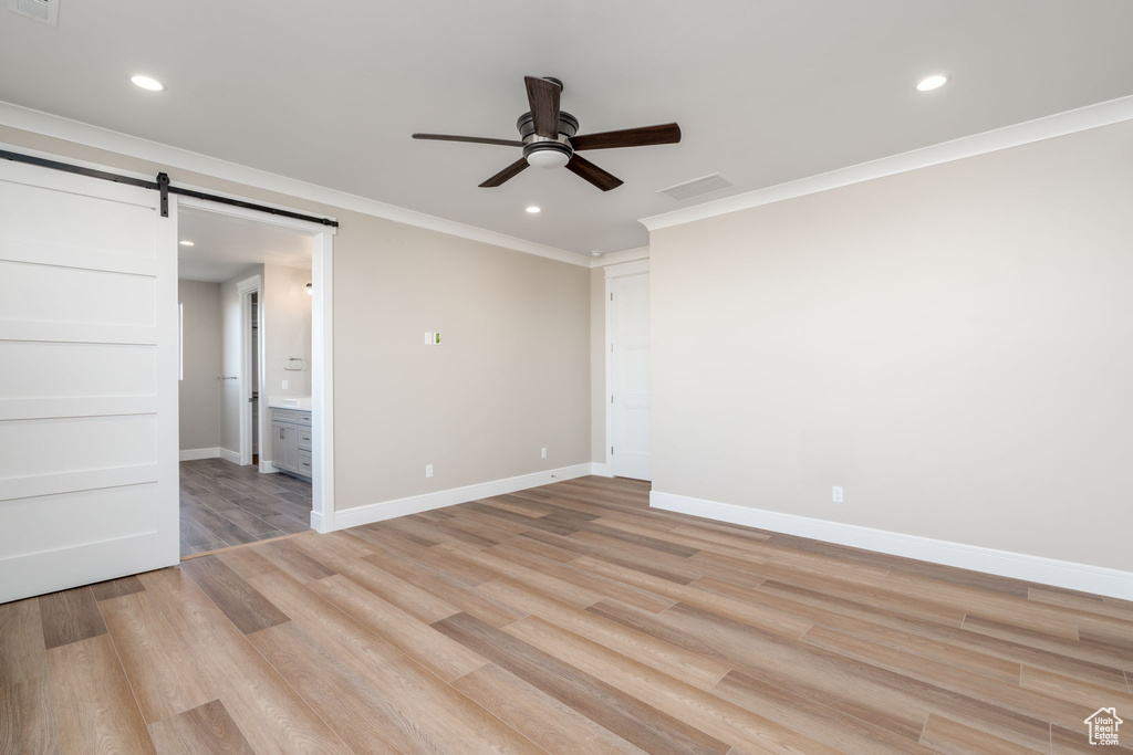 Unfurnished bedroom featuring a barn door, light wood-type flooring, ornamental molding, recessed lighting, and baseboards