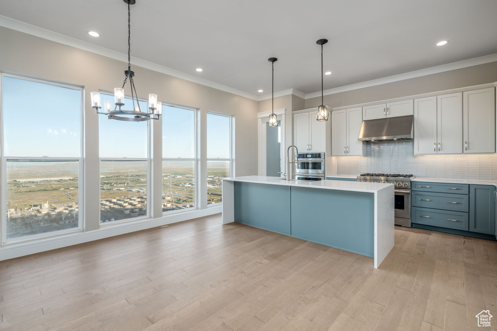 Kitchen featuring under cabinet range hood, stainless steel appliances, light countertops, light wood-type flooring, and a chandelier