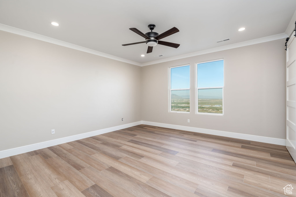 Empty room with a barn door, ceiling fan, ornamental molding, recessed lighting, and light wood-style flooring