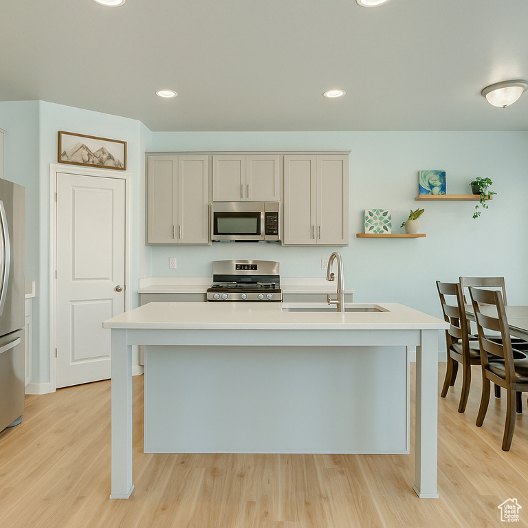 Kitchen featuring appliances with stainless steel finishes, open shelves, a sink, light countertops, and light wood-style flooring