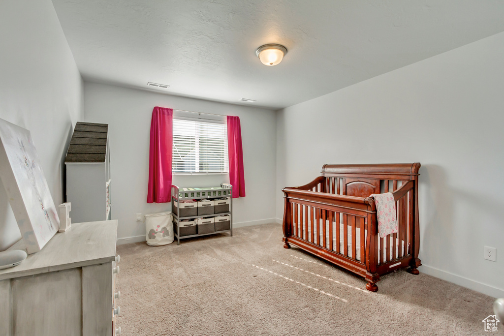 Carpeted bedroom featuring visible vents, baseboards, and a nursery area