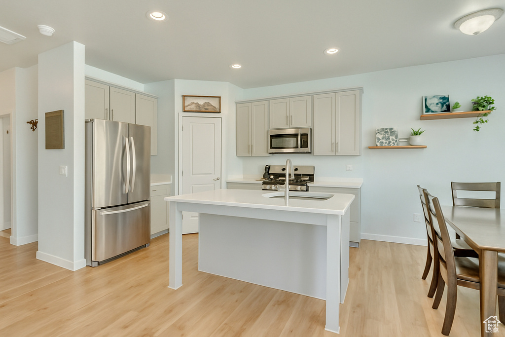 Kitchen featuring open shelves, light countertops, baseboards, light wood-style floors, and stainless steel appliances