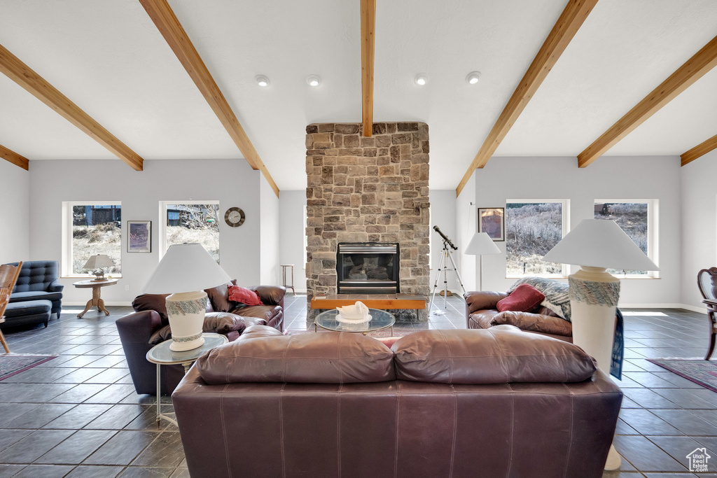 Living room featuring dark tile patterned floors, beam ceiling, a wealth of natural light, and a fireplace