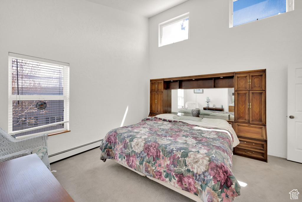 Bedroom with a baseboard heating unit, light carpet, and a towering ceiling