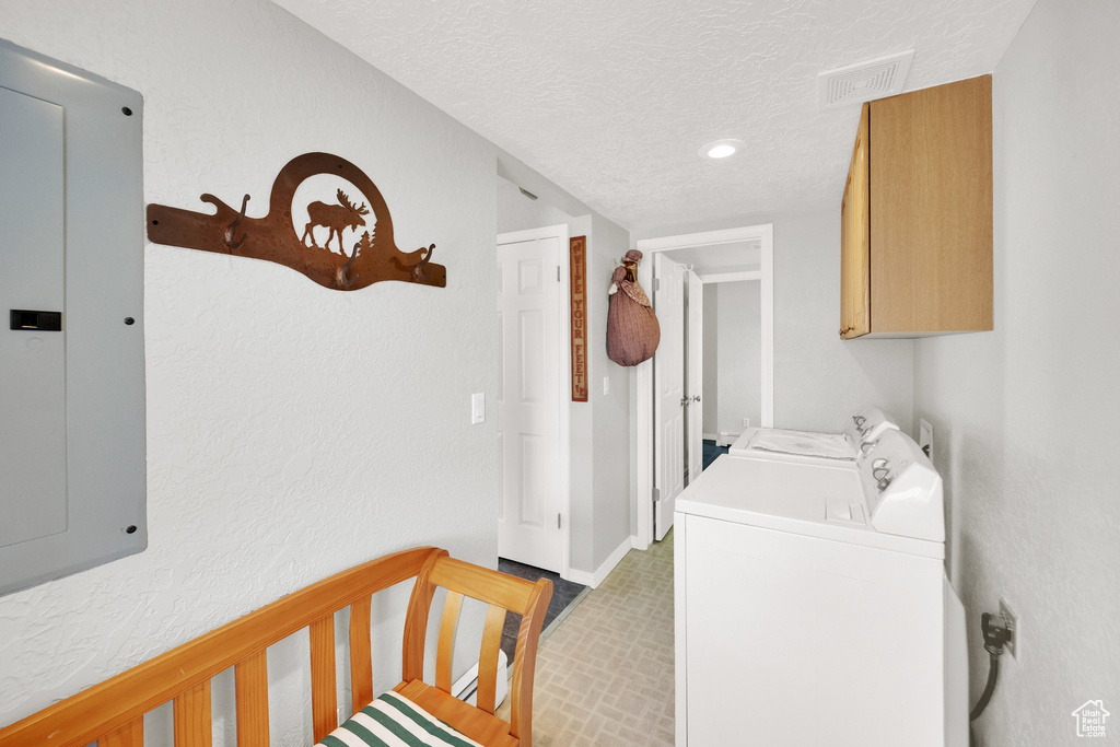 Clothes washing area with electric panel, independent washer and dryer, a textured ceiling, visible vents, and cabinet space