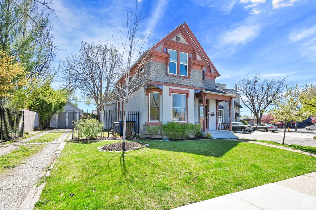 Victorian-style house featuring an outbuilding, a shed, a front yard, and fence