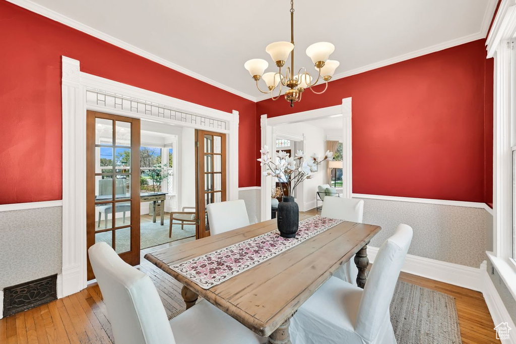 Dining area featuring visible vents, a notable chandelier, light wood-style floors, crown molding, and french doors
