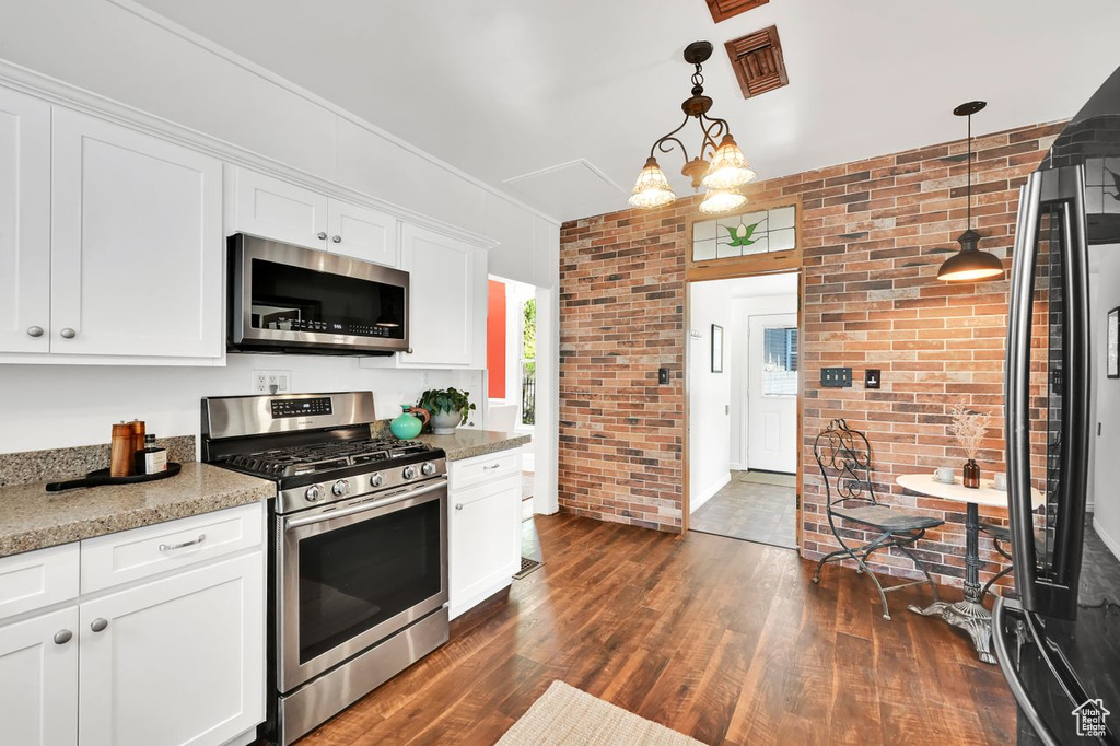 Kitchen with visible vents, white cabinets, brick wall, dark wood-style floors, and stainless steel appliances