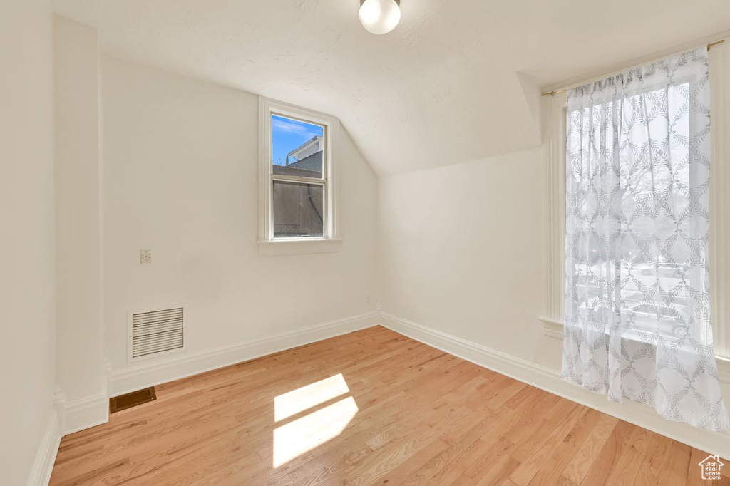 Additional living space featuring visible vents, baseboards, vaulted ceiling, and wood finished floors