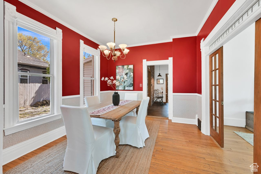 Dining space with a notable chandelier, light wood-type flooring, ornamental molding, and a healthy amount of sunlight