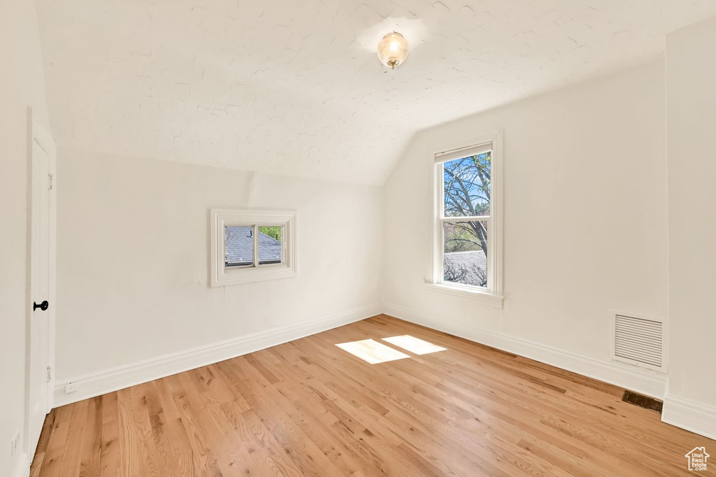 Additional living space with visible vents, baseboards, light wood-type flooring, and lofted ceiling
