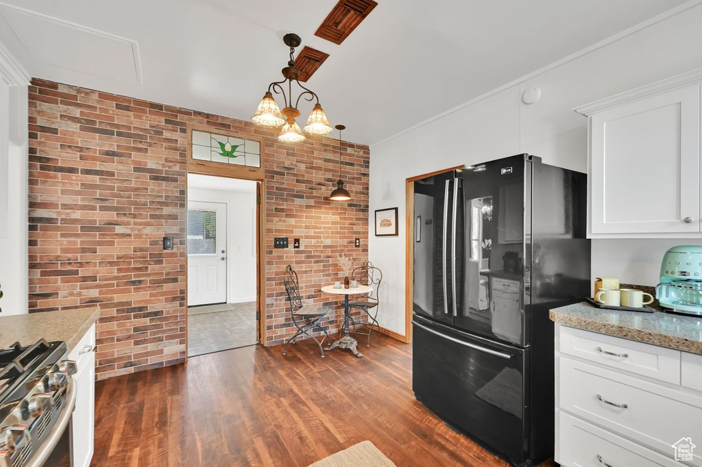 Kitchen with stainless steel range with gas cooktop, freestanding refrigerator, dark wood finished floors, white cabinetry, and brick wall