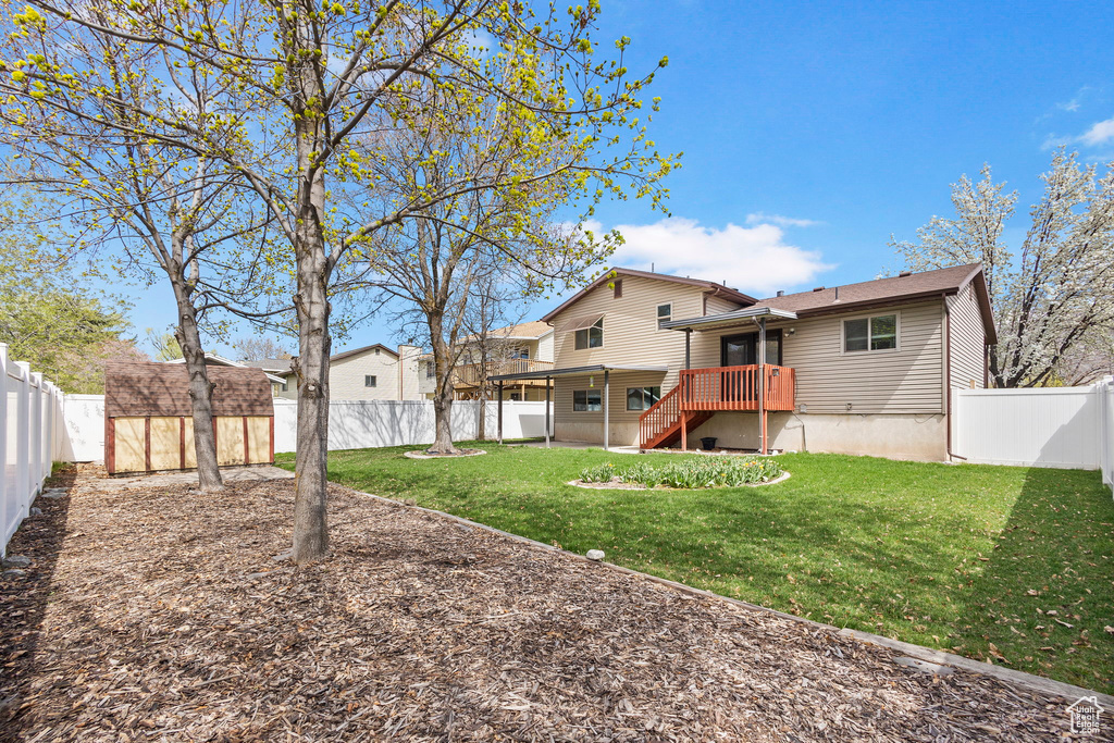Back of property with a lawn, a fenced backyard, a storage shed, and an outbuilding