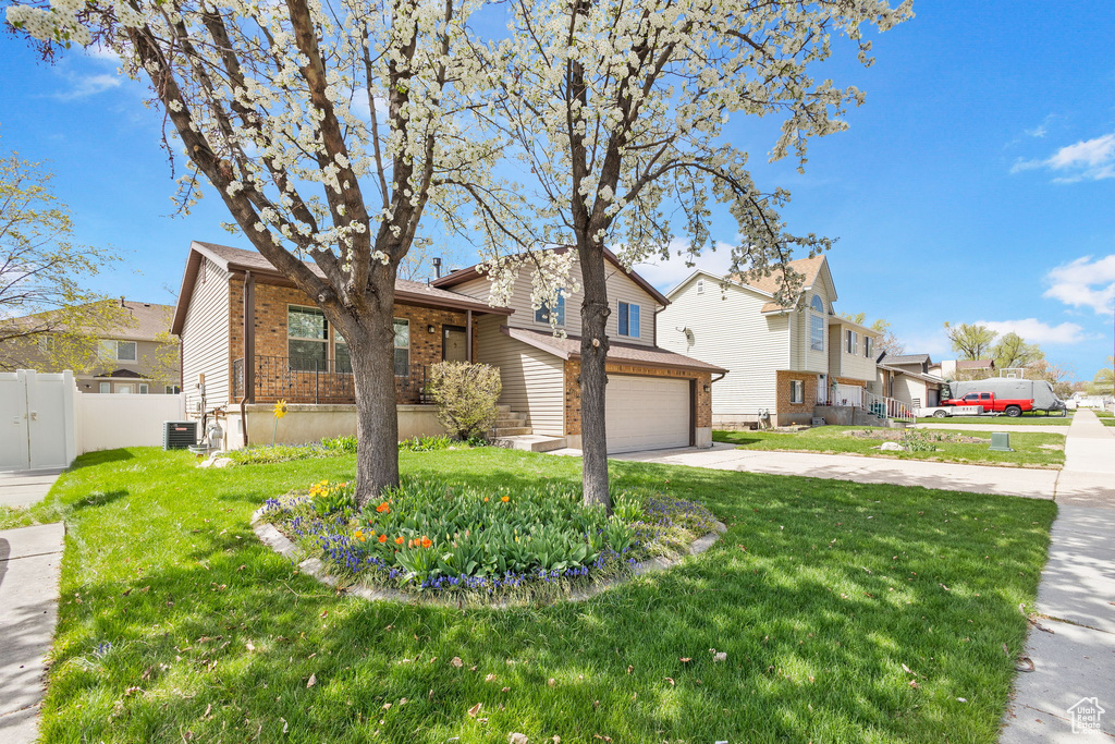 View of front of property with driveway, an attached garage, a front lawn, brick siding, and fence