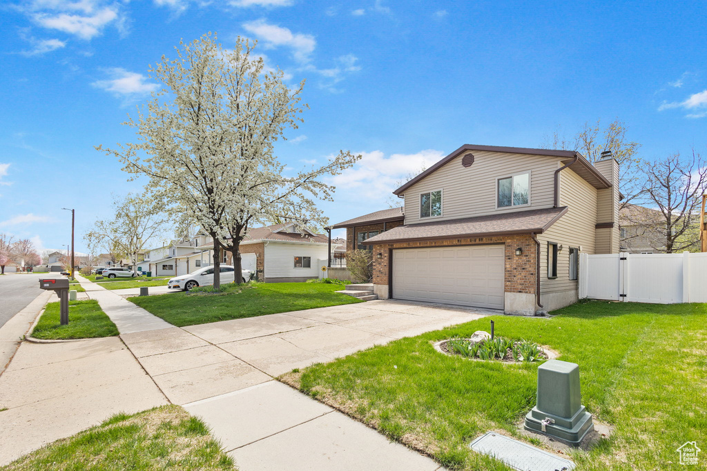 View of front of property featuring a front yard, an attached garage, a chimney, brick siding, and driveway