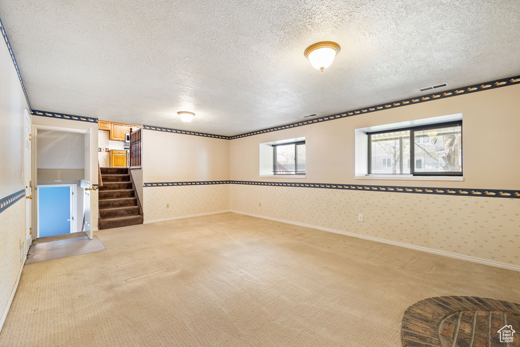 Below grade area featuring visible vents, stairway, light carpet, and a textured ceiling