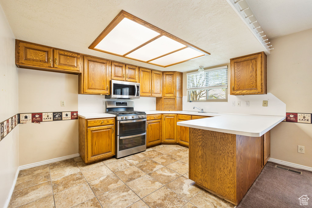 Kitchen featuring stainless steel appliances, a peninsula, brown cabinets, and baseboards