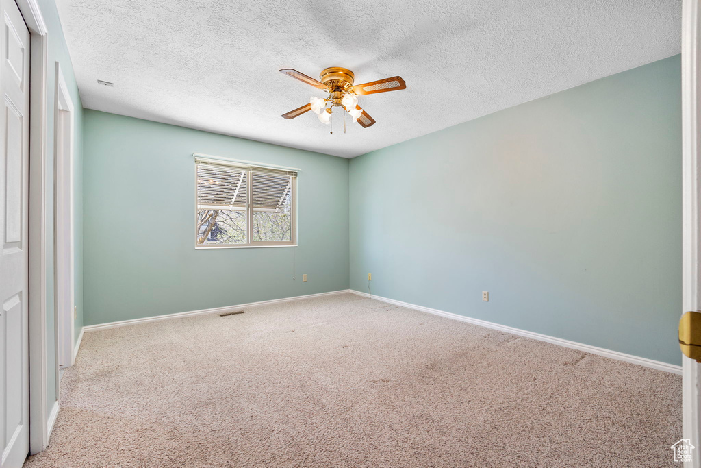 Carpeted empty room with a textured ceiling, ceiling fan, baseboards, and visible vents
