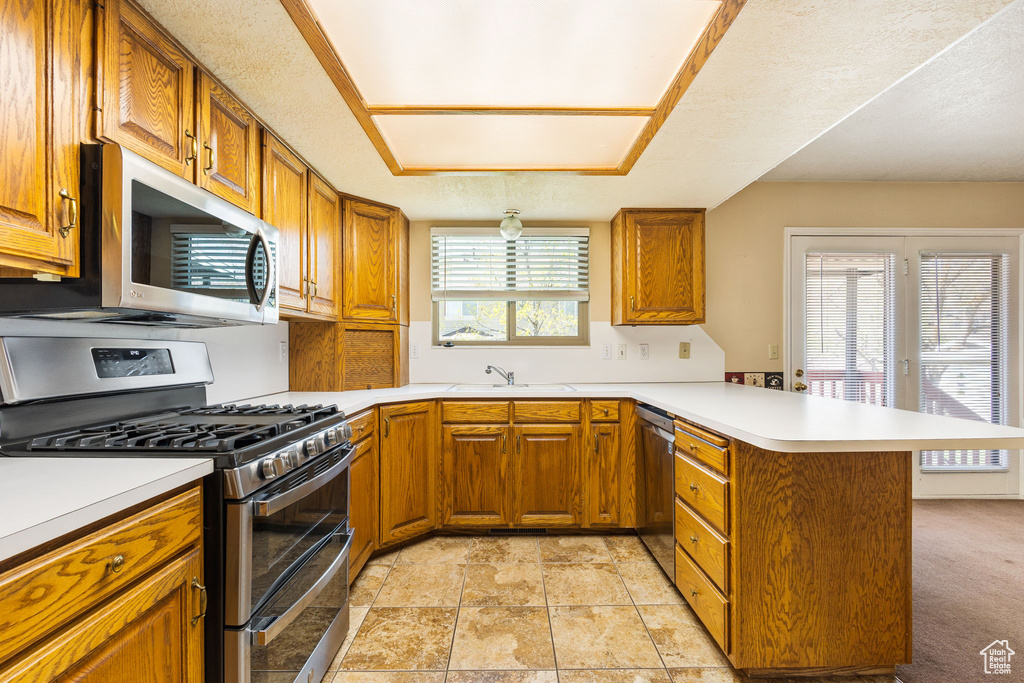 Kitchen with brown cabinets, light countertops, appliances with stainless steel finishes, and a peninsula