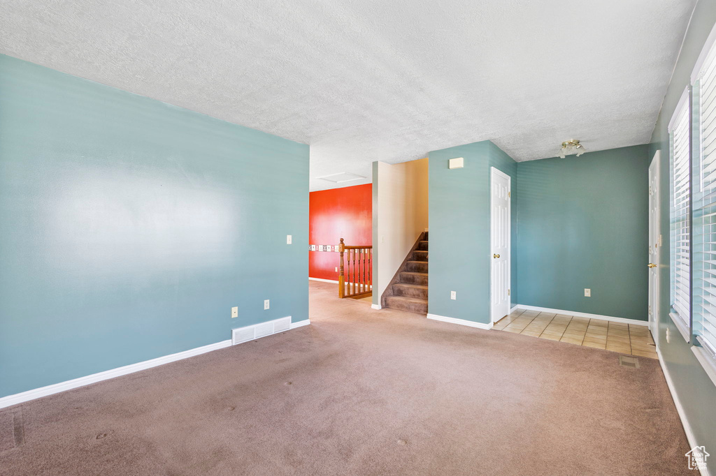 Empty room featuring baseboards, stairway, a textured ceiling, carpet floors, and visible vents